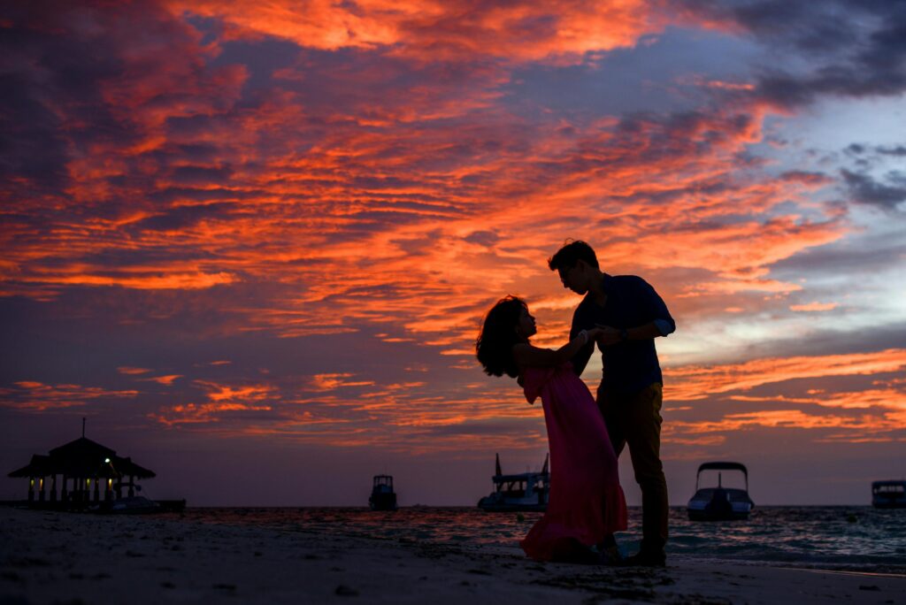 Silhouetted couple sharing a romantic moment on the beach during a stunning sunset.