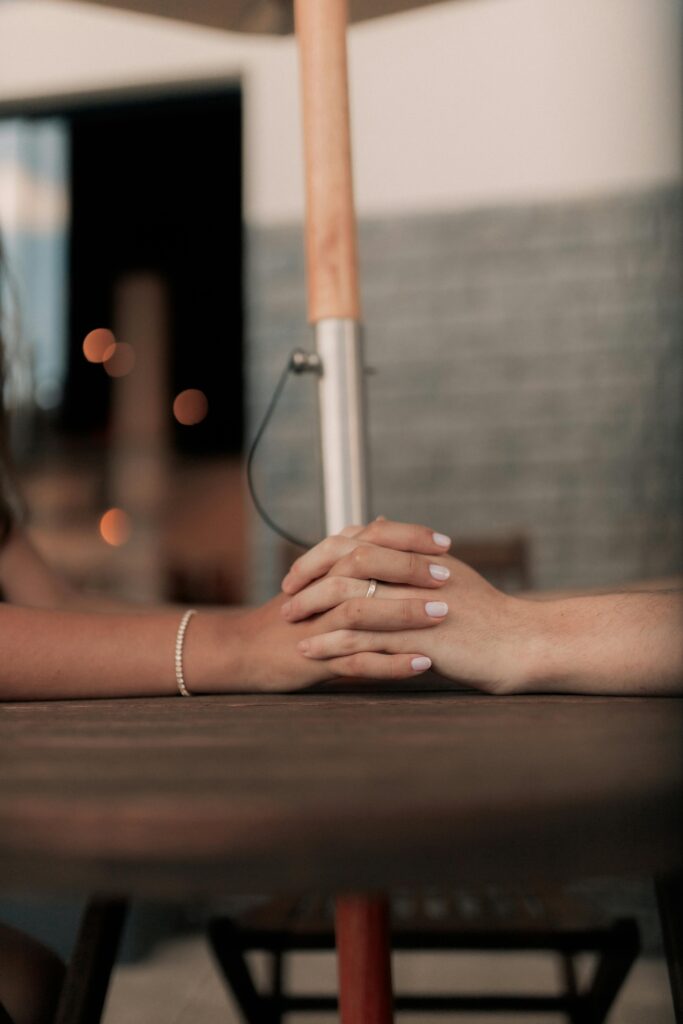 Close-up of two hands romantically clasped at an outdoor cafe table.