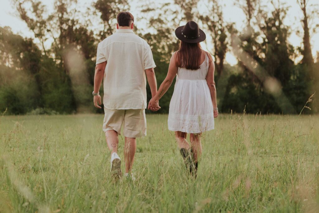 A couple strolls through a sunny field, embodying love and togetherness.