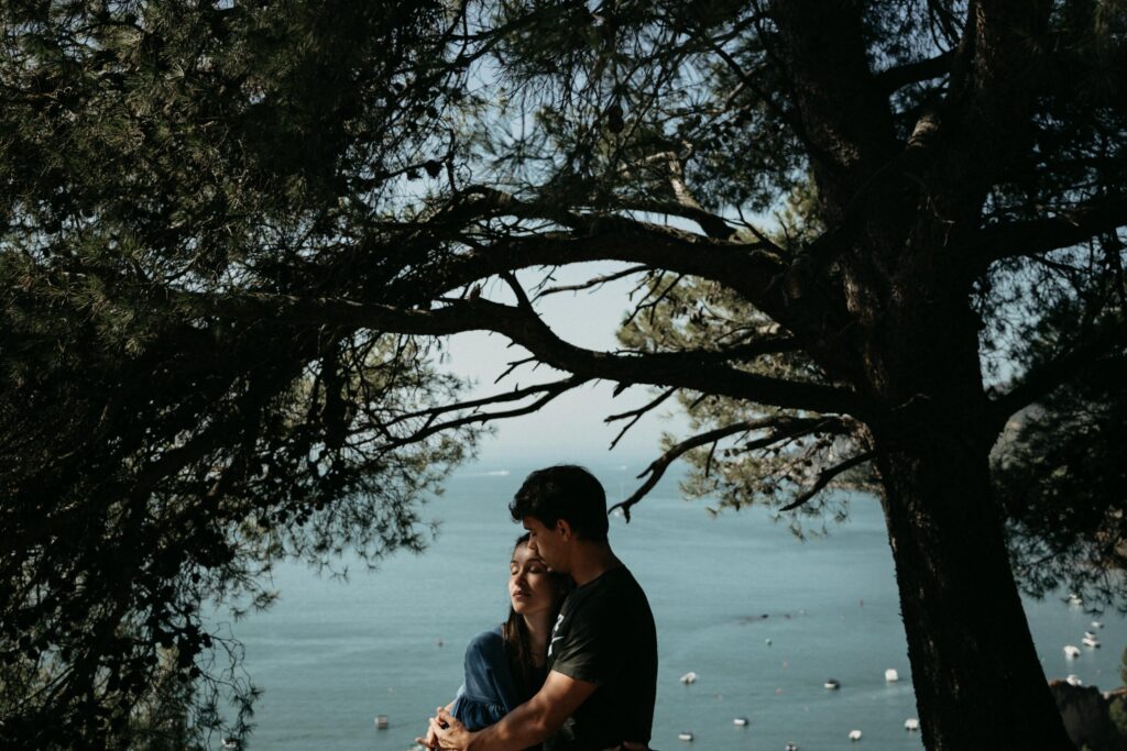 A couple embracing under trees with a scenic ocean view, conveying love and tranquility.