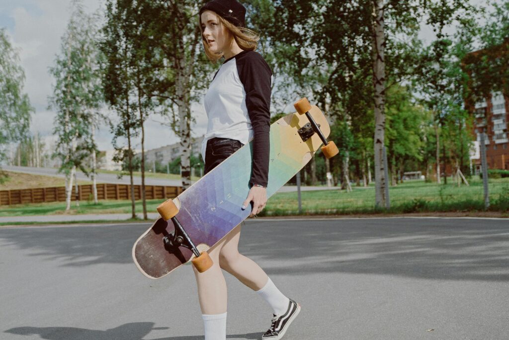 Teen girl carrying a longboard skateboard in an urban park, enjoying outdoor leisure activities.