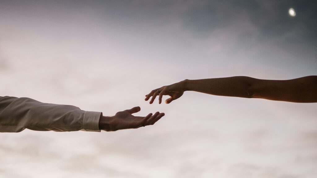 Two hands reaching towards each other against a soft twilight sky symbolizing connection and love.
